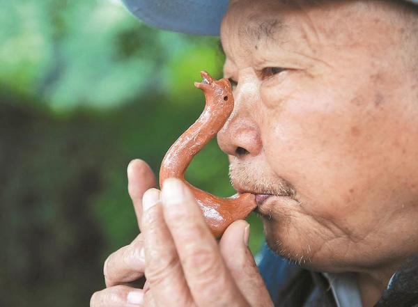 萬富冊老人為過往市民吹奏泥鵝子。